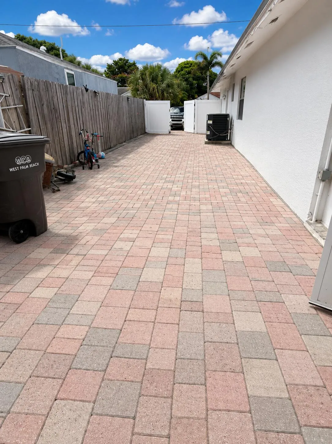 Paver driveway bordered by a wood fence and white vinyl fencing