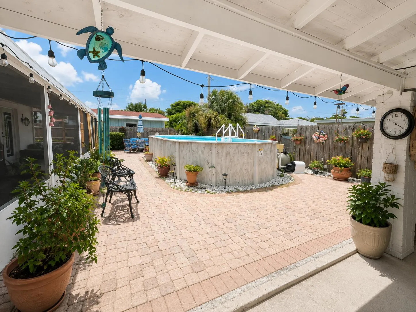 Paver patio with an above-ground pool, covered patio area, and perimeter fencing