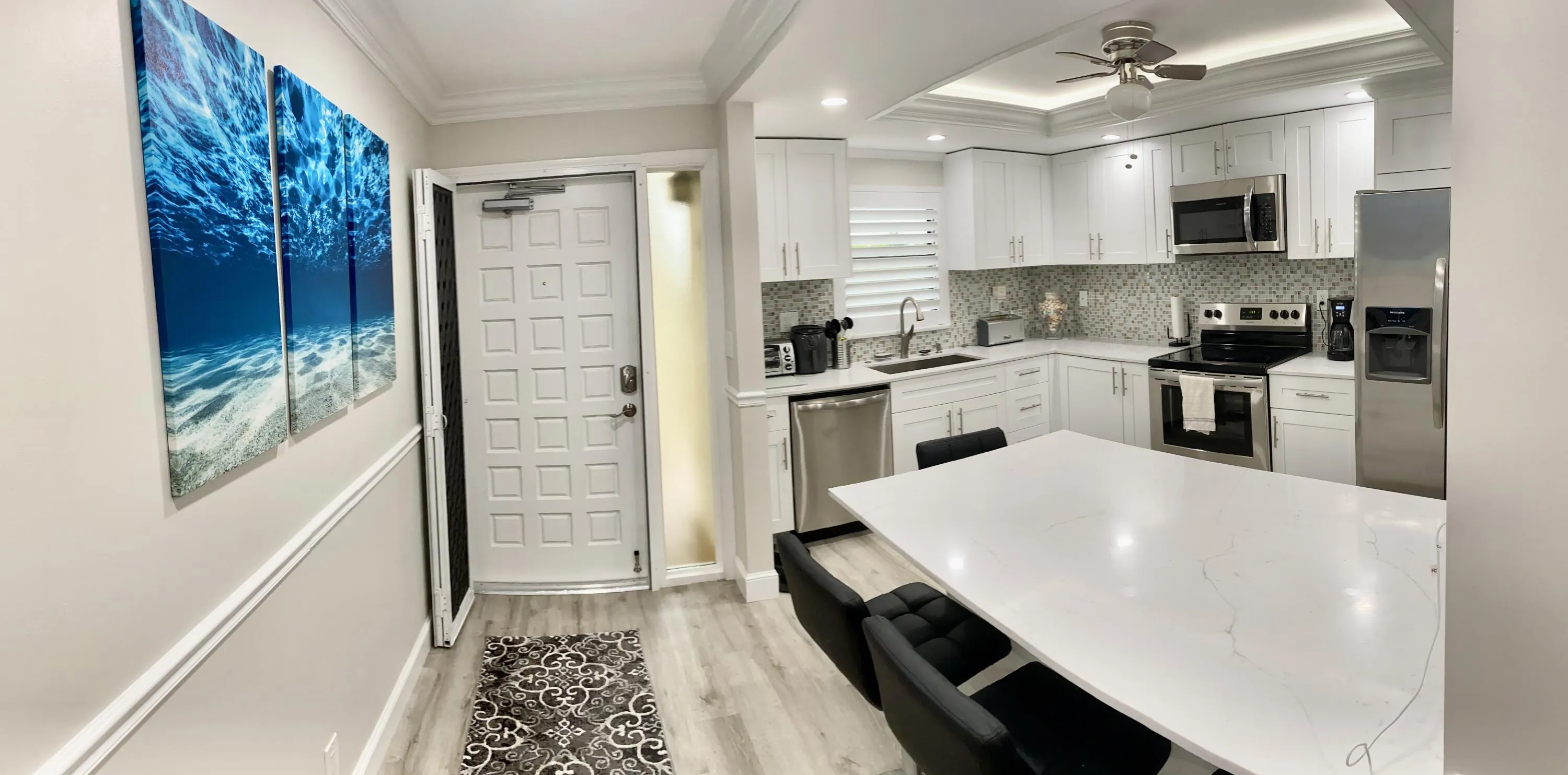 Modern kitchen featuring white cabinetry, stainless steel appliances, a white quartz island, and wood-finish flooring