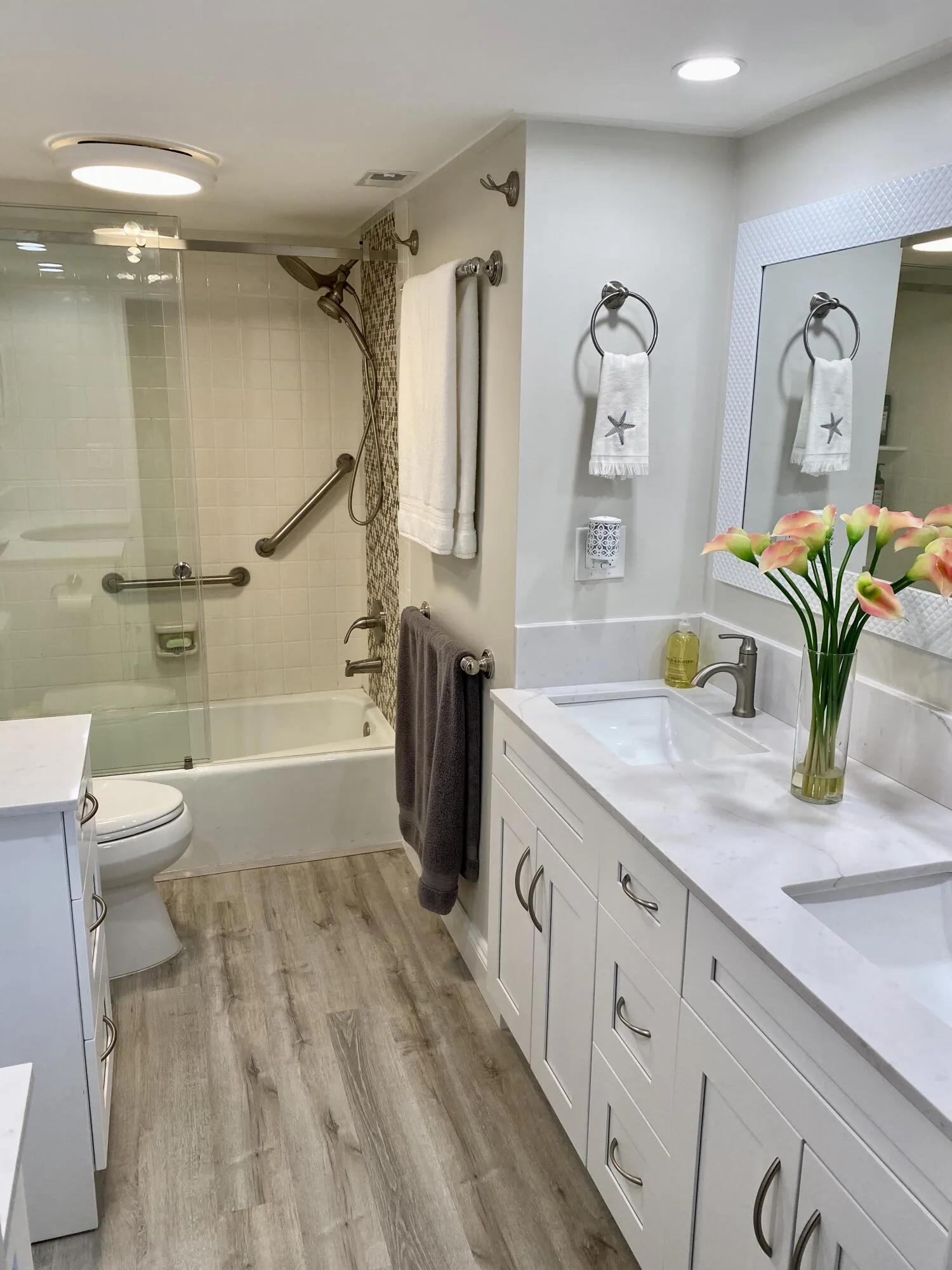 White double vanity with integrated sinks, wood-finish flooring, glass-enclosed shower, and a framed mirror