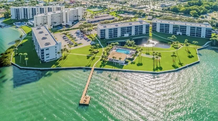 Waterfront community featuring multiple modern residential buildings with manicured landscaping, mature palm trees, and resort-style amenities including a swimming pool and spa