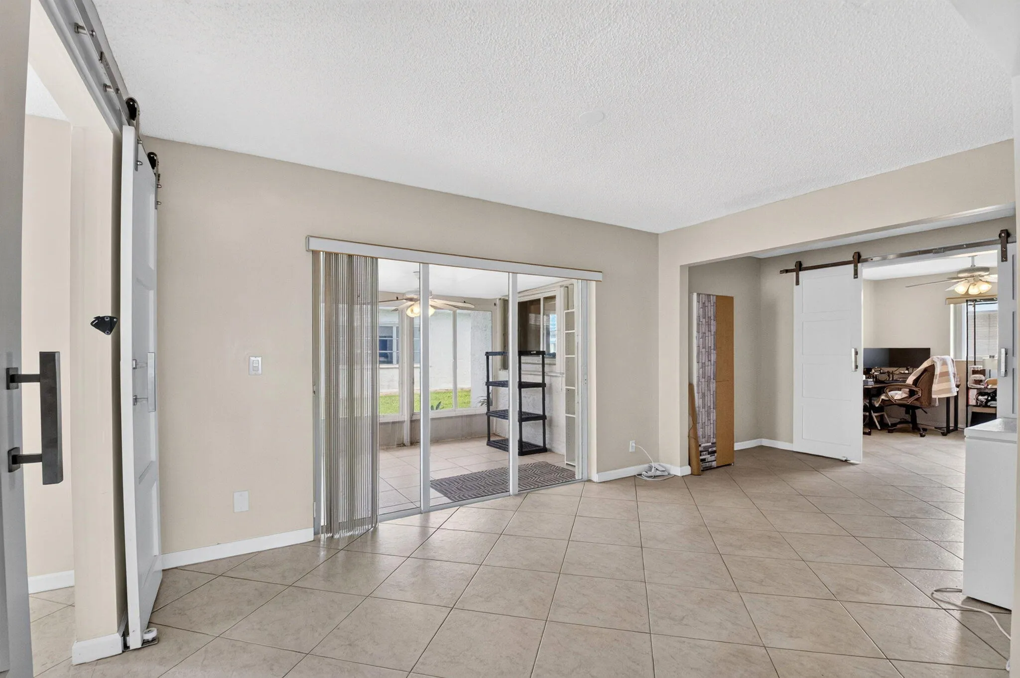 Tile flooring throughout, white barn doors, and glass sliding doors opening to an enclosed patio