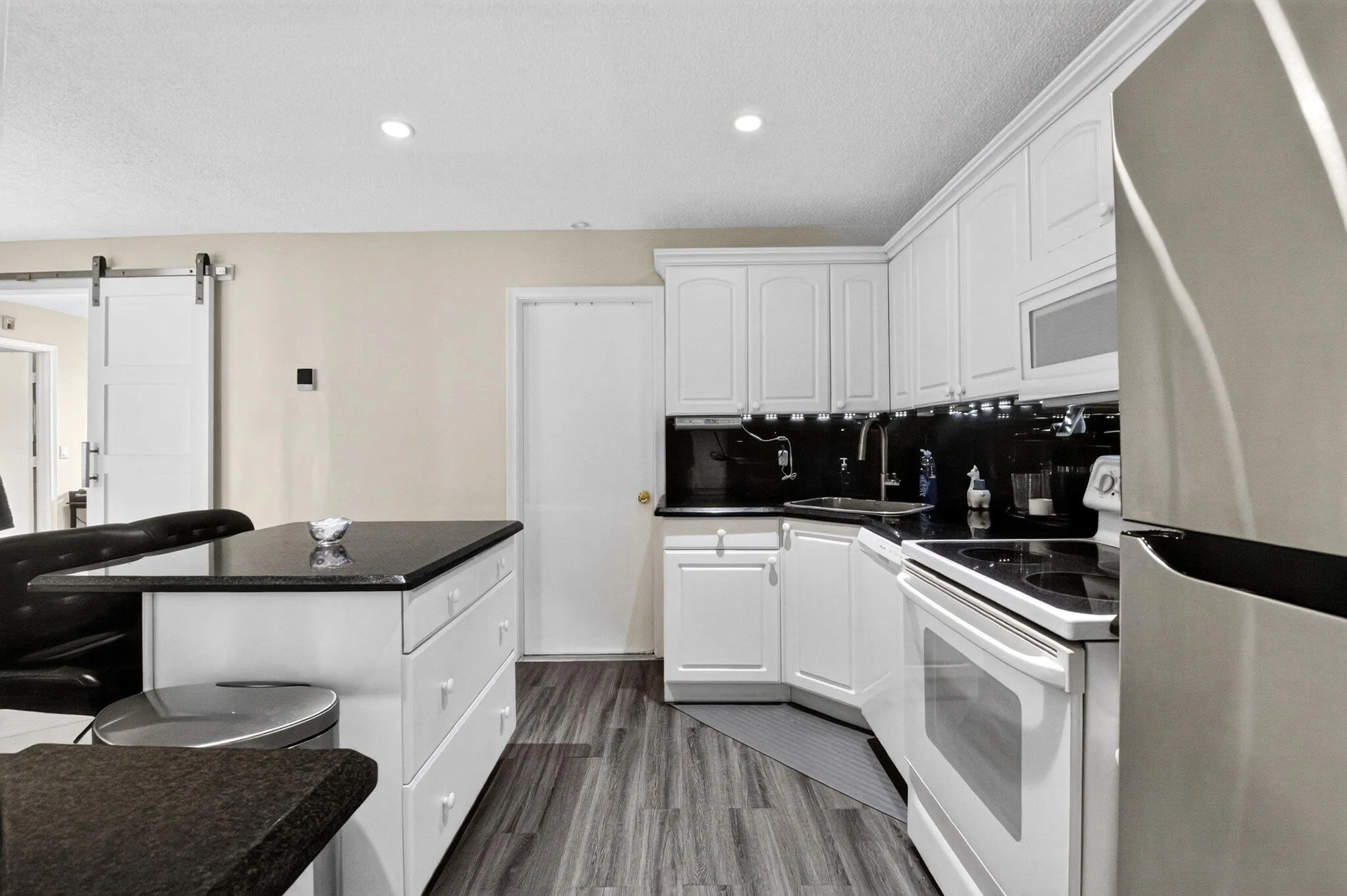 Modern kitchen featuring white cabinetry with paneled doors, stainless steel appliances including a double wall oven, black granite countertops, and a curved island with seating