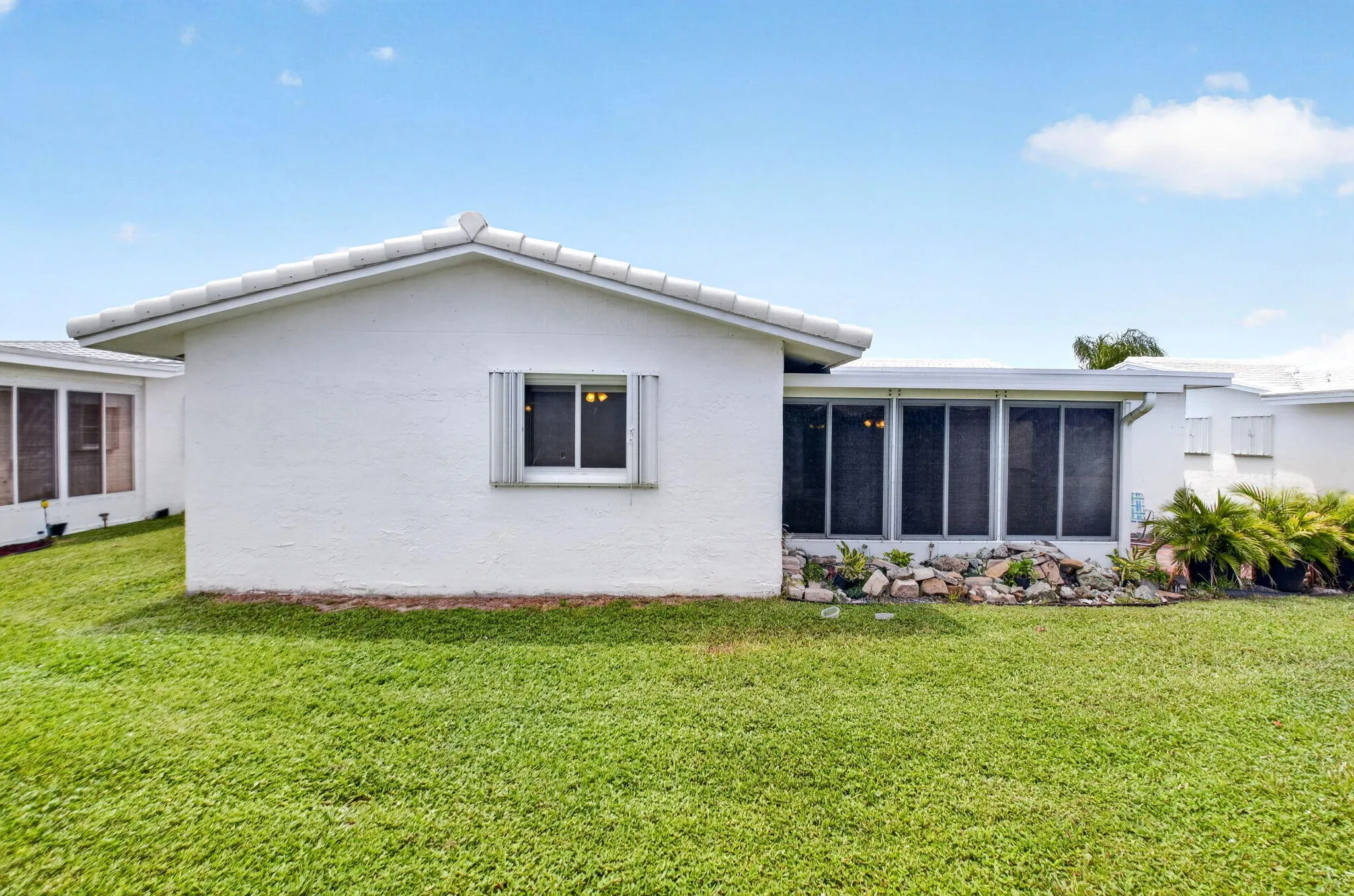 Expansive lawn with an attached screened enclosure, white exterior, and a rock garden landscaping feature
