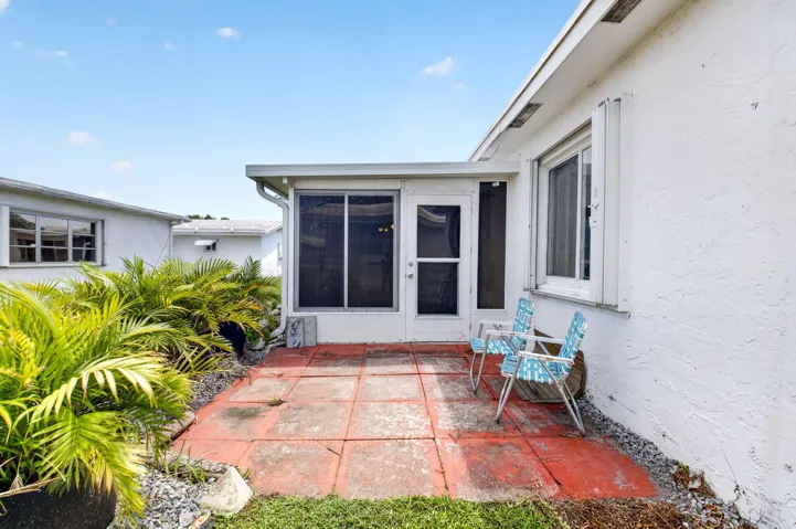 Enclosed patio space with concrete flooring, accented by lush tropical landscaping and white exterior siding