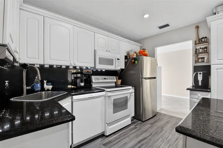 White cabinetry with crown molding, dark speckled countertops, stainless steel sink, under-cabinet lighting, and wood-finish flooring