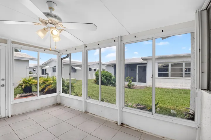 Screened enclosure featuring a ceiling fan with integrated lighting, tile flooring, and multiple window panels