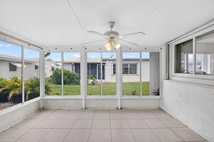 Screened enclosure with ceramic tile flooring, ceiling fan with integrated lighting, and multiple windows
