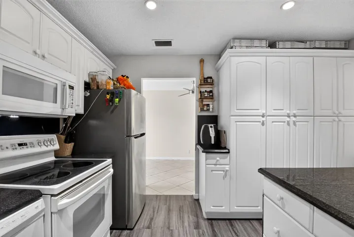 White cabinetry with brushed nickel hardware, dark stone-finish countertops, wood-finish flooring, recessed lighting, and stainless steel appliances