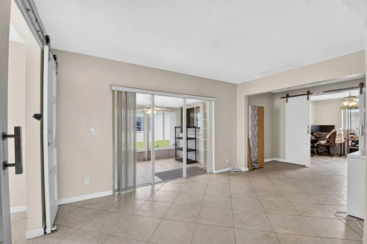 Tile flooring throughout, white barn doors, and glass sliding doors opening to an enclosed patio