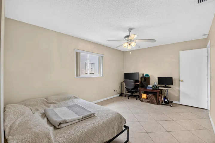 Light-colored tile flooring, window with blinds, ceiling fan with integrated lighting, and a white interior door