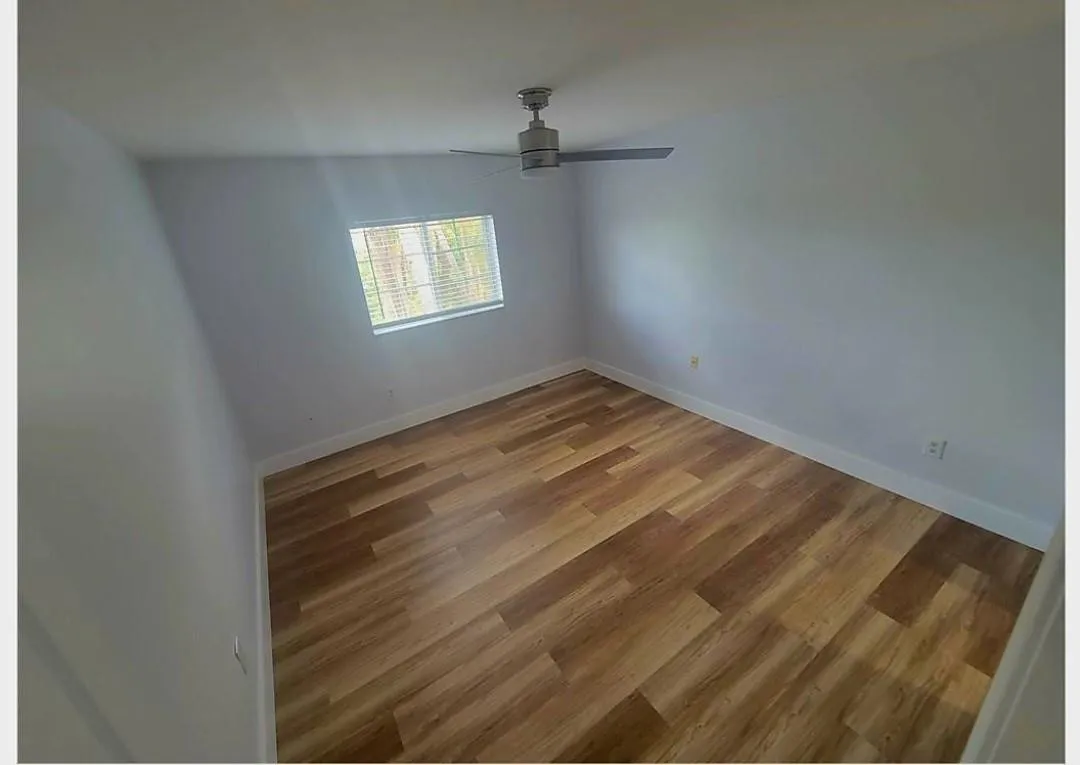 Expansive room featuring wood-finish flooring, a window with blinds, and a ceiling-mounted fan