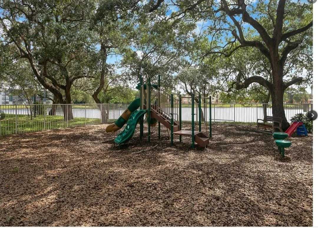 Playground with a slide, monkey bars, and a climbing structure, surrounded by mature trees