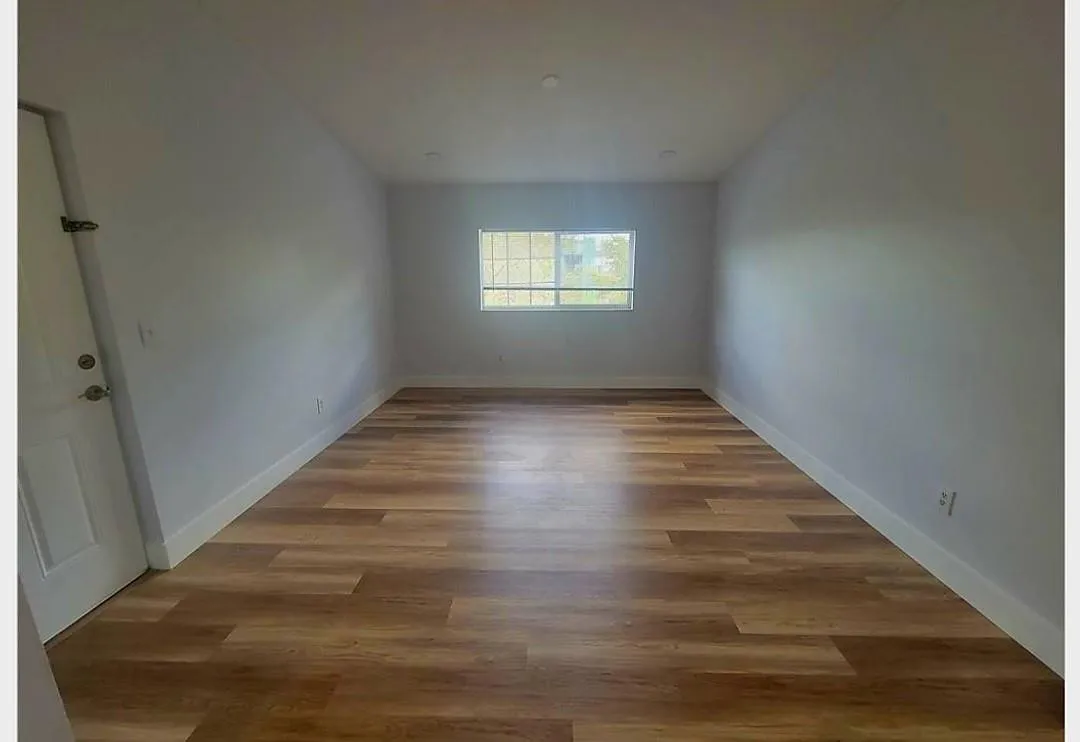 Wood-finish flooring with white baseboards, recessed ceiling lighting, and a window with security bars