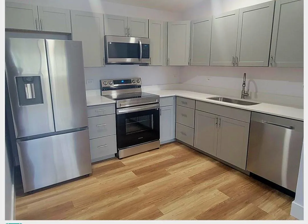 Kitchen featuring wood-finish flooring, light grey cabinetry, white countertops, and stainless steel appliances