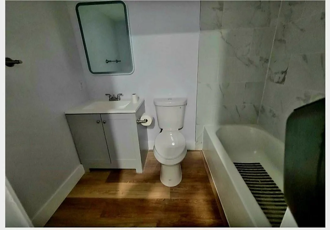 Bathroom featuring a vanity with integrated sink, white toilet, and a bathtub with tiled surround