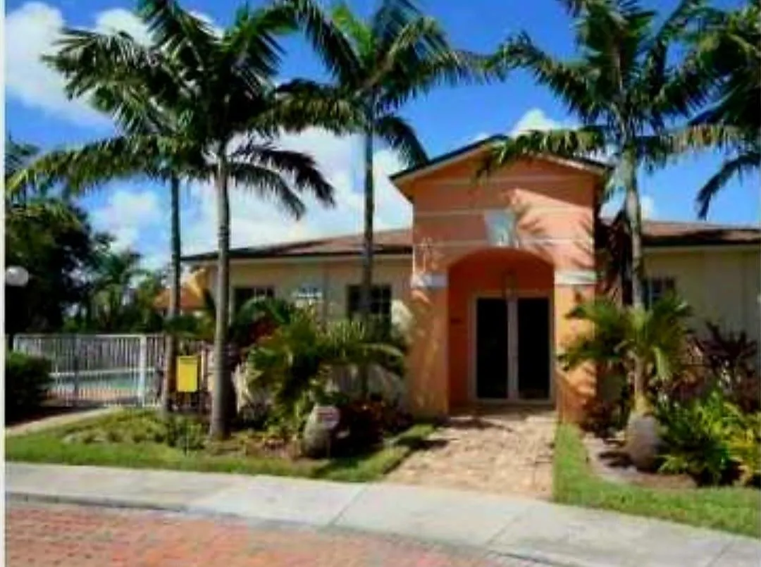 Arched entryway with double doors, paver walkway, mature palm trees, and established landscaping