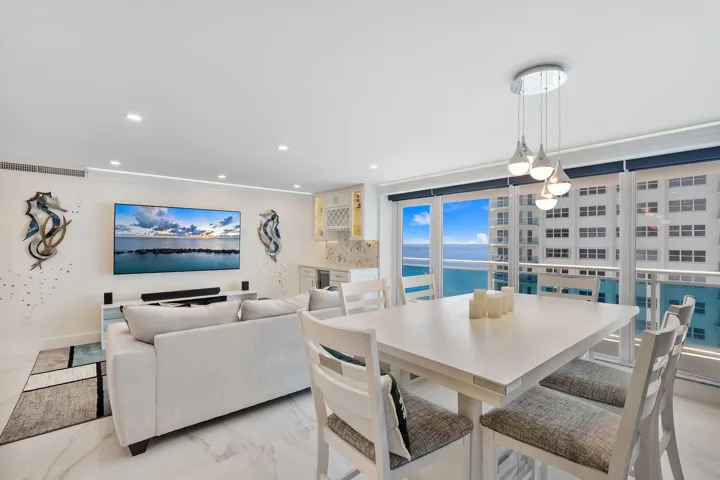 Expansive window wall with balcony access, recessed lighting, white wood-finish flooring, built-in wet bar with wine storage, and a modern dining chandelier