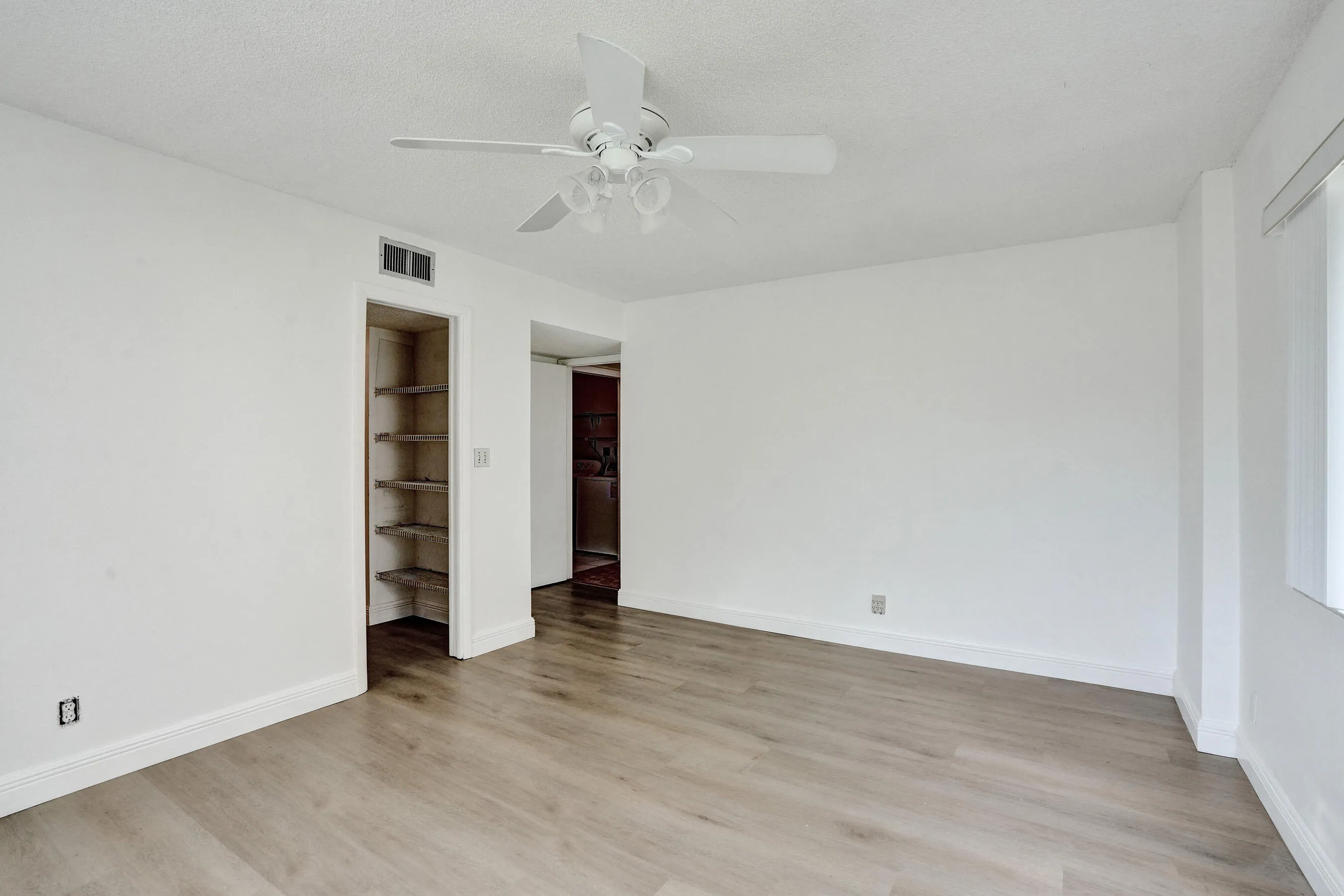 Wood-finish flooring throughout, white walls, built-in shelving, and a ceiling fan with integrated lighting