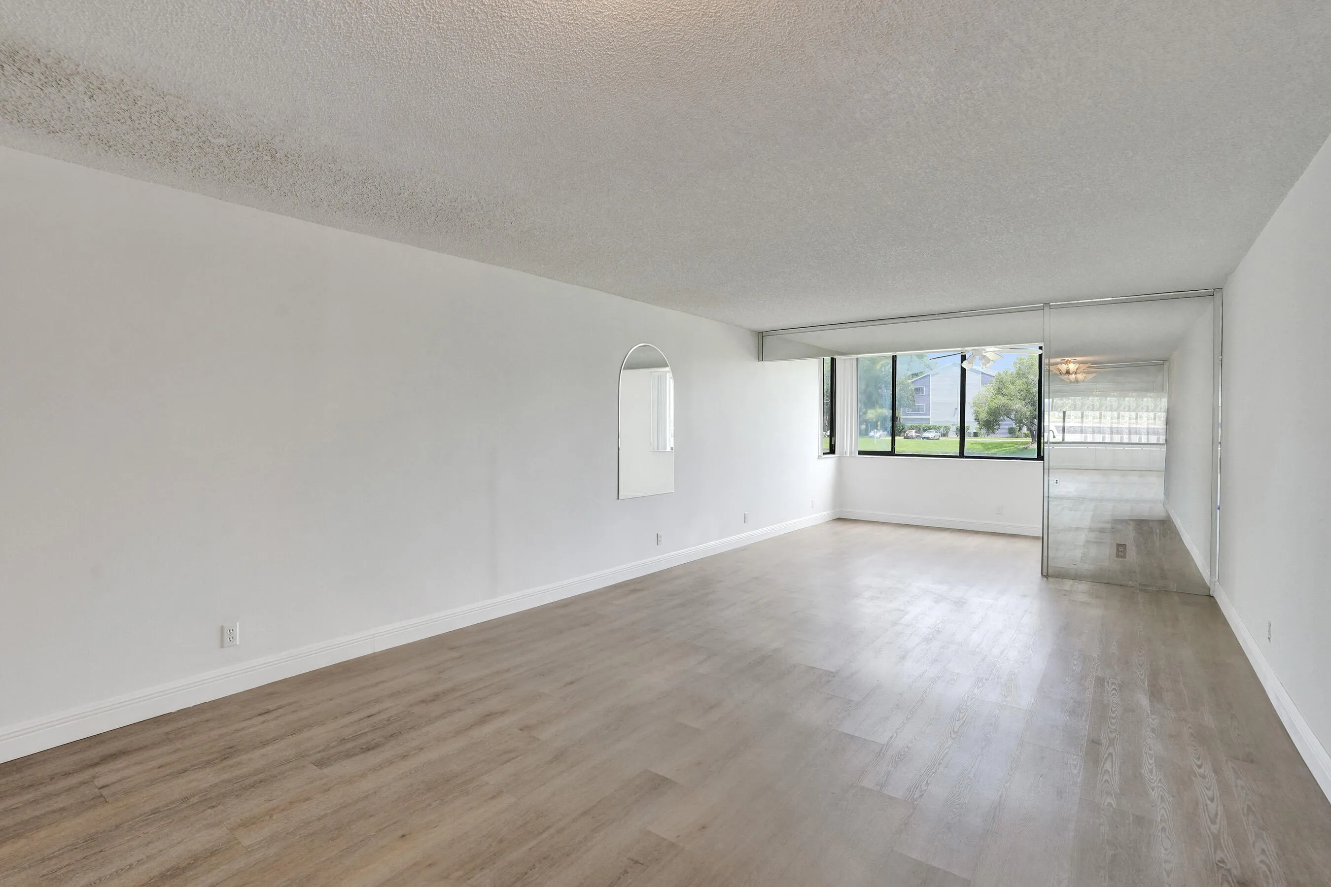 Wood-finish flooring throughout, white walls, large window with outdoor scenery, and mirrored wall feature