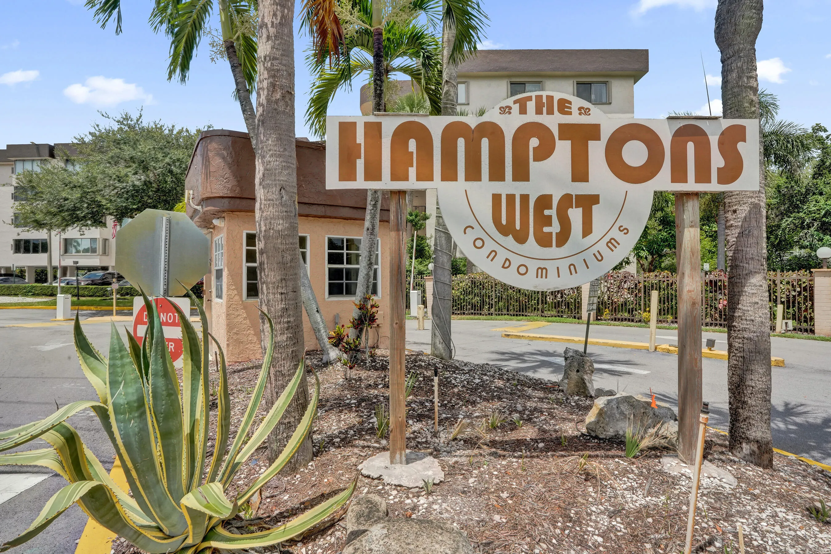 The Hamptons West Condominiums entrance sign with a security booth and established landscaping