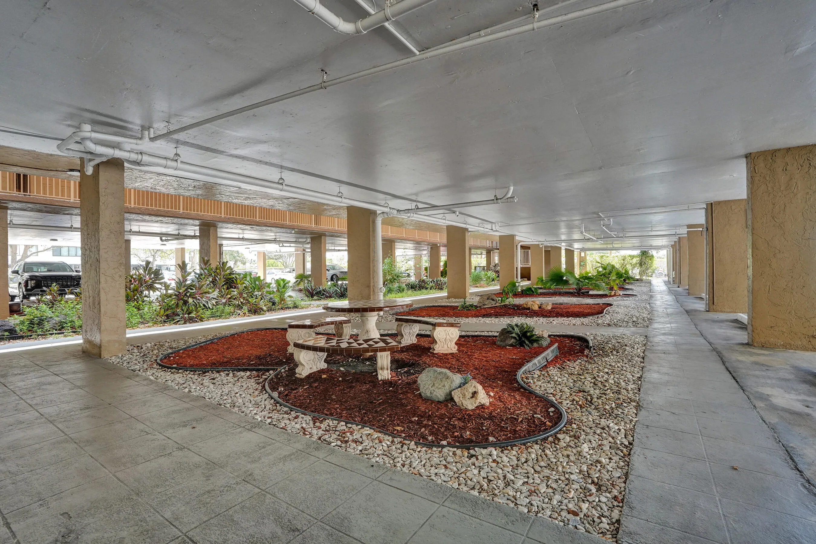 Covered outdoor area featuring decorative stone pathways, landscaped garden beds with red mulch, and a built-in stone picnic table