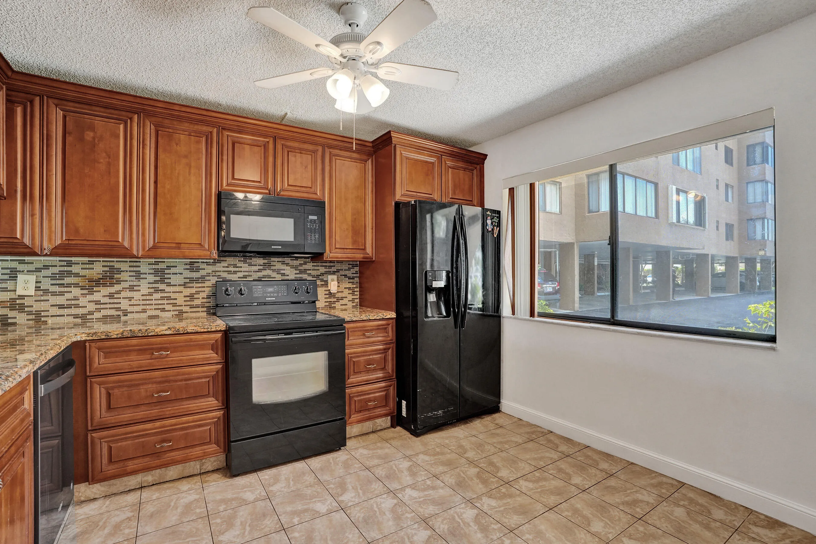 Kitchen featuring wood cabinetry, tile backsplash, stone-finish countertops, black appliances, and a ceiling fan