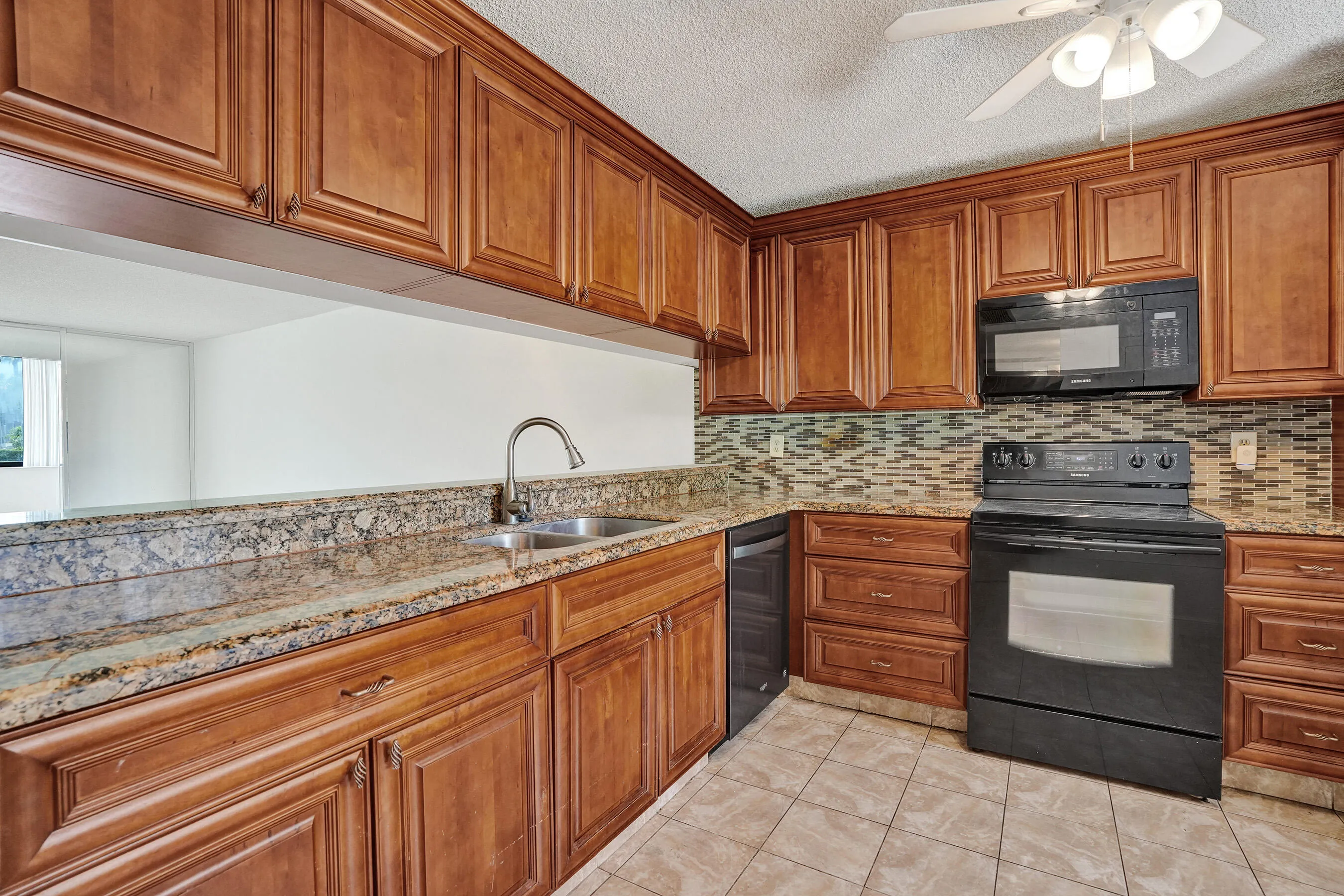 Kitchen featuring wood cabinetry, stone countertops, stainless steel sink, black appliances, and tile flooring