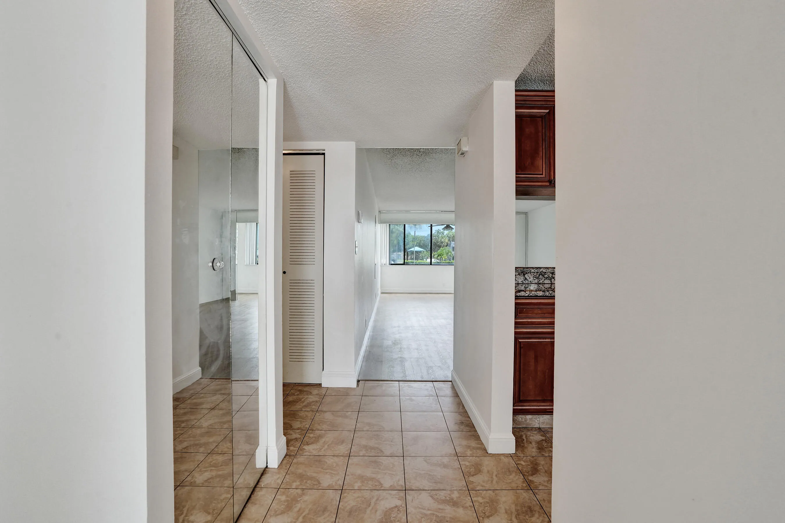 Hallway featuring tile flooring, mirrored closet doors, a louvered closet door, and wood-finish cabinetry with a countertop