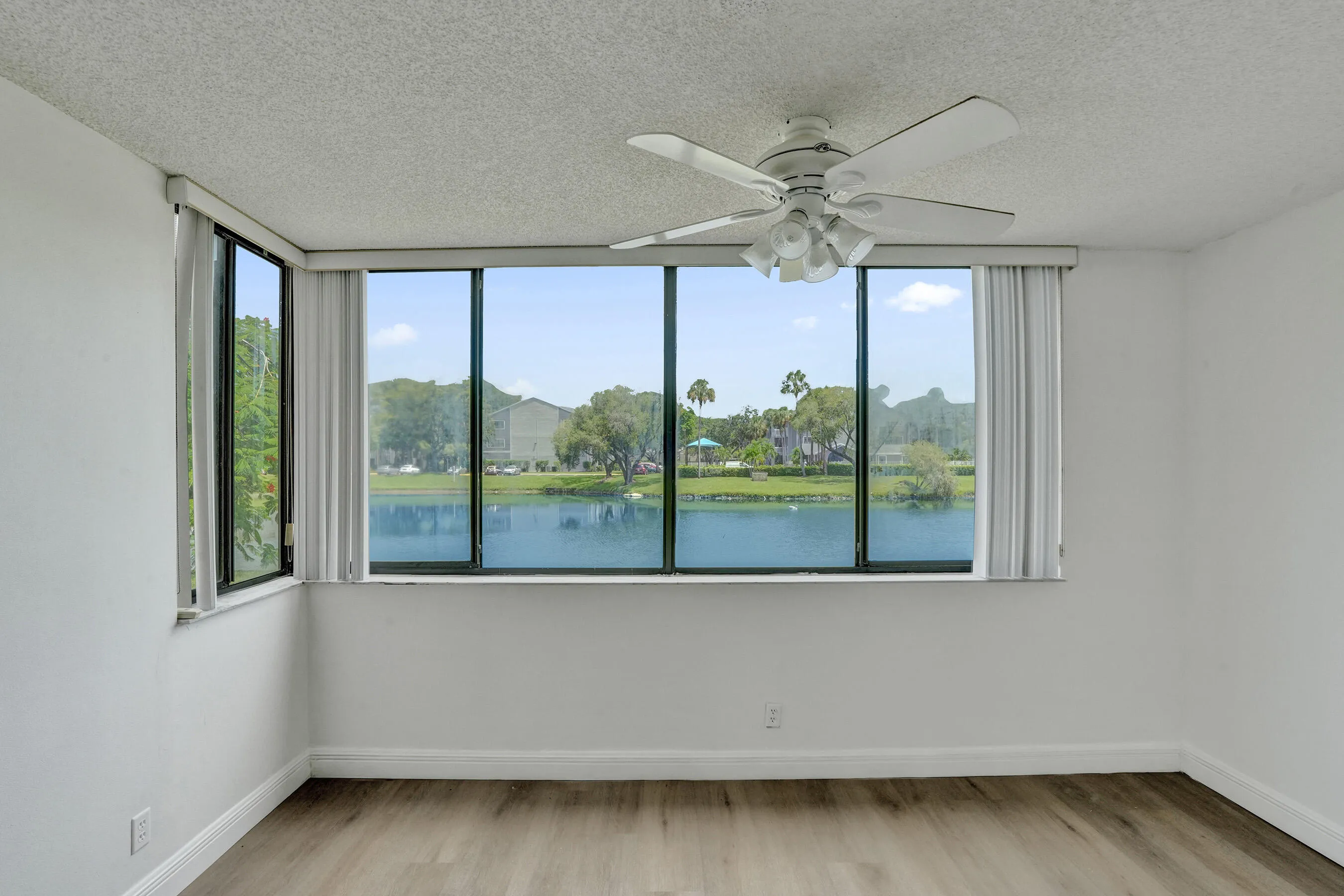 Wall-to-wall windows with a water backdrop, wood-finish flooring, and a ceiling fan with integrated lighting