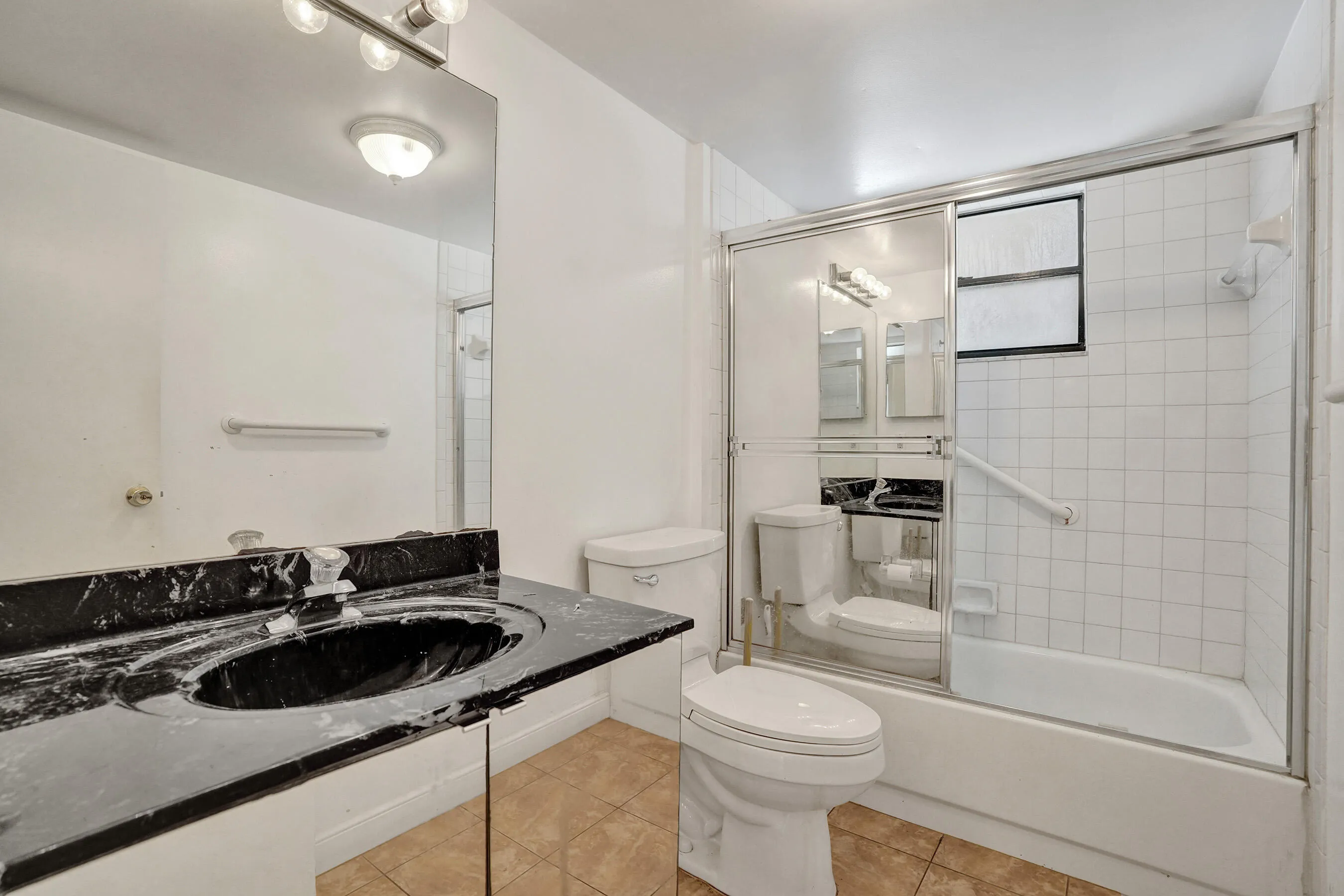 Black countertop vanity with an integrated sink, full-width mirror, tile flooring, and a shower-tub combination with a sliding glass enclosure