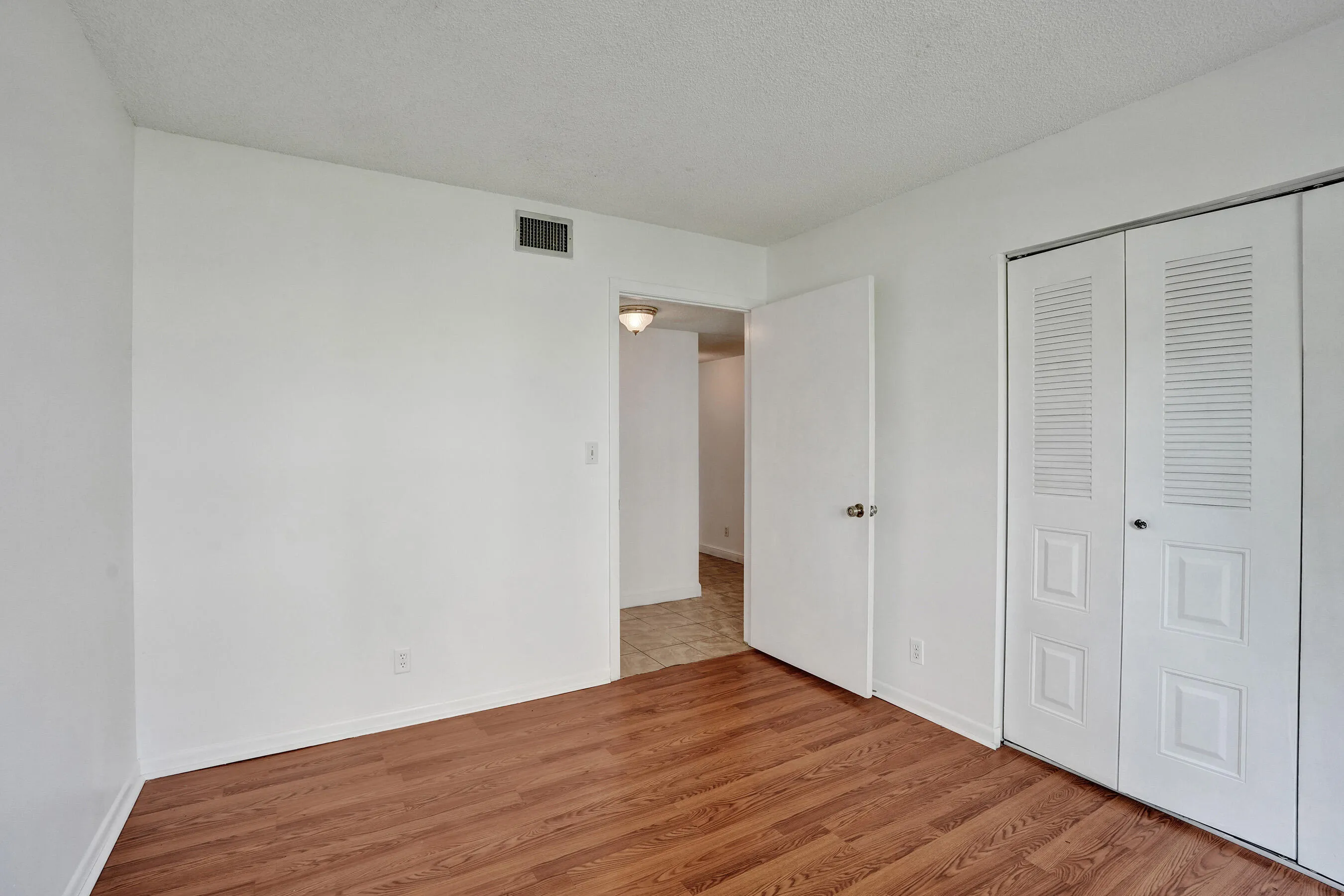 Wood-finish flooring with white baseboards, white walls, and a white six-panel door
