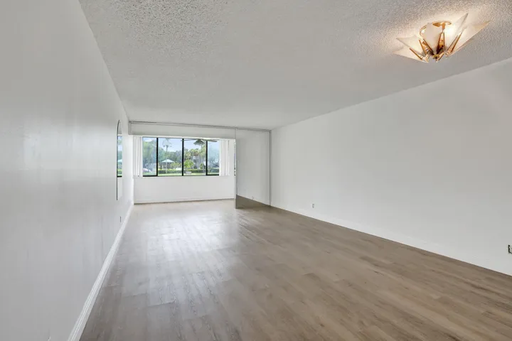 Expansive room with wood-finish flooring, white walls, and a large window offering abundant light