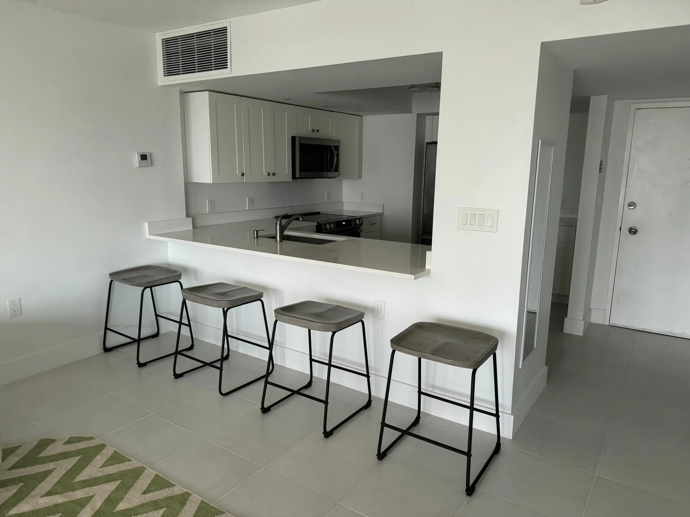 Open-concept kitchen with white shaker cabinetry, stainless steel appliances, and a pass-through bar with seating