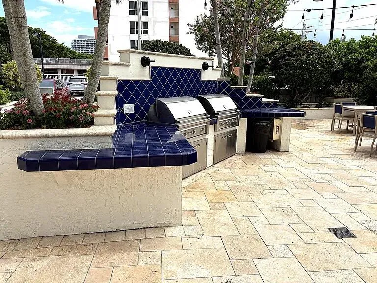 Outdoor kitchen featuring two built-in stainless steel grills, a tiled countertop, and a patterned tile backsplash