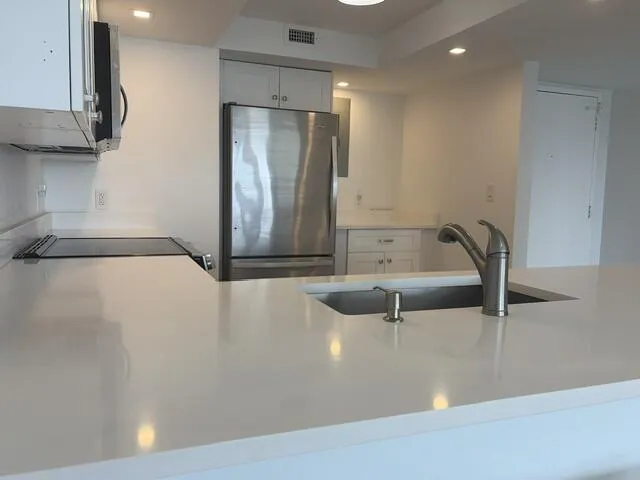 White countertops, integrated sink, stainless steel faucet, stainless steel refrigerator, and recessed lighting