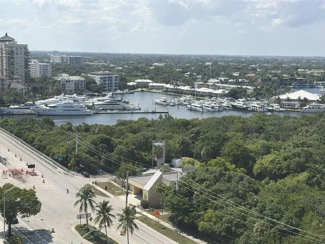 Waterfront marina with multiple vessels, surrounded by lush green foliage and urban structures