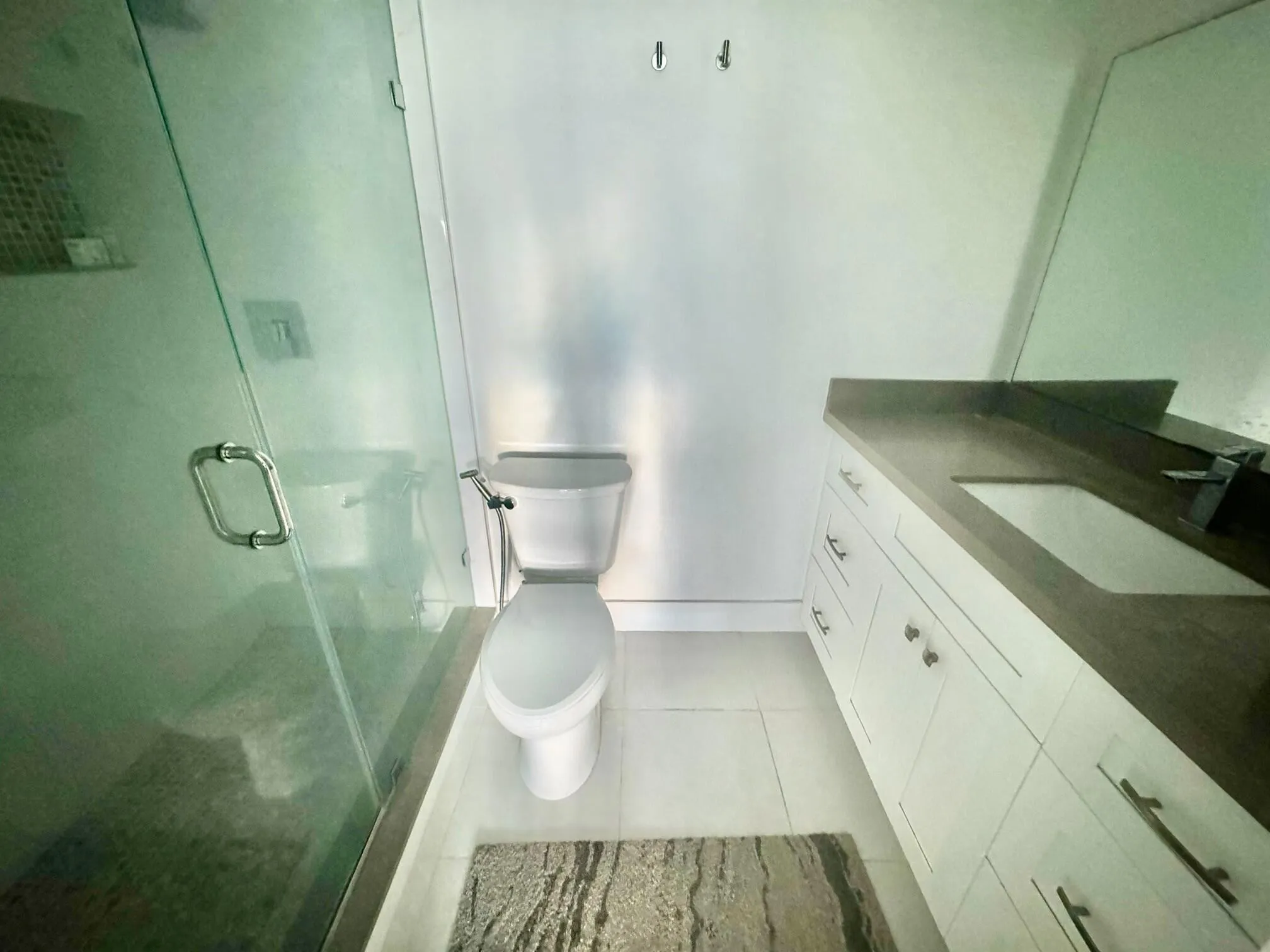 Frameless glass shower enclosure, white vanity with rectangular under-mount sink, dark stone-finish countertop, matte black faucet, and white floor tiling
