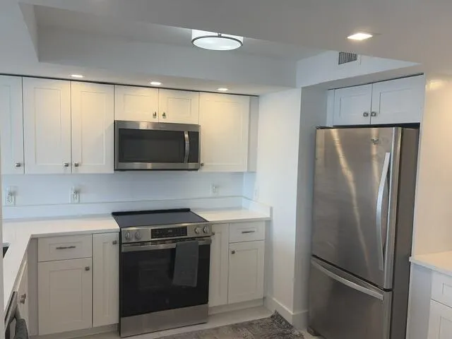 White shaker-style cabinetry with stainless steel hardware, white countertops, built-in microwave, stainless steel range, and stainless steel refrigerator