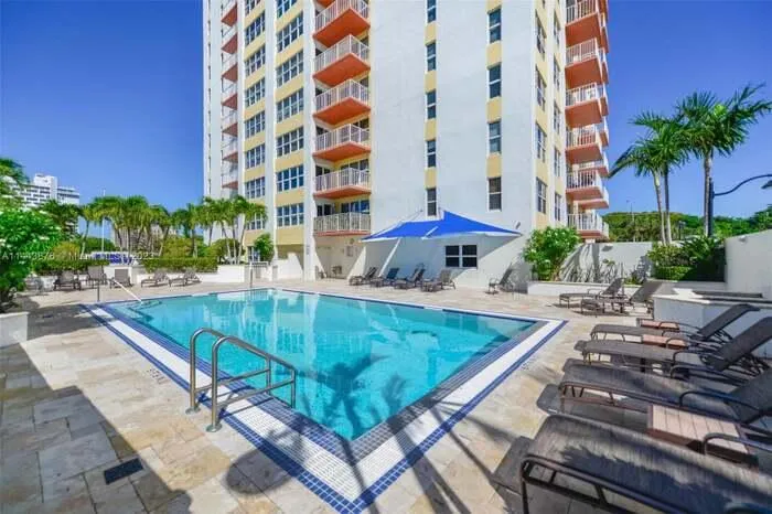 Outdoor pool with blue and white tile border, surrounded by light-colored pavers, and mature palm trees
