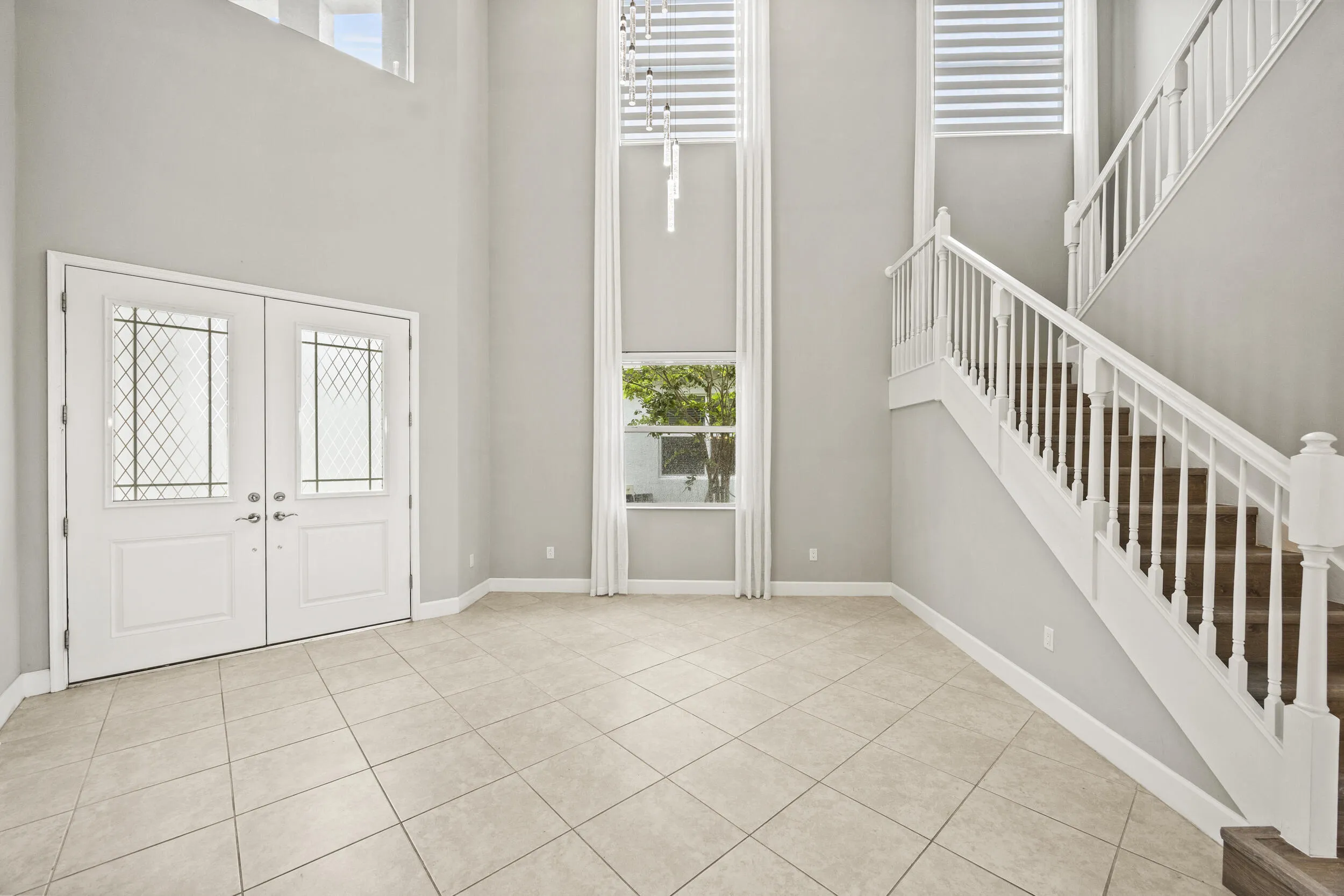 Two-story entry with double doors featuring decorative glass inserts, ceramic tile flooring, and a grand staircase with white railings