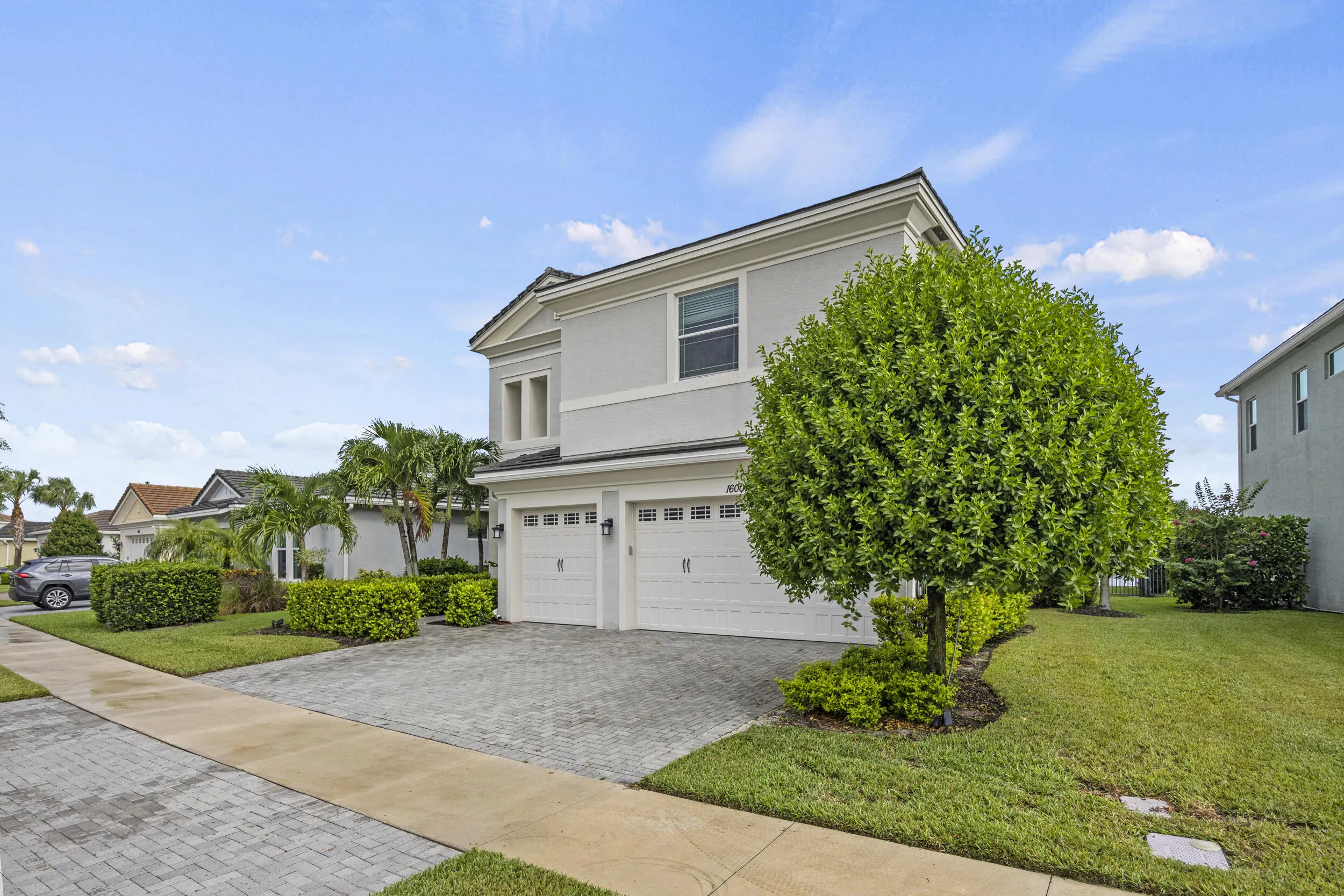 Two-story exterior with a two-car garage, paver driveway, and mature landscaping