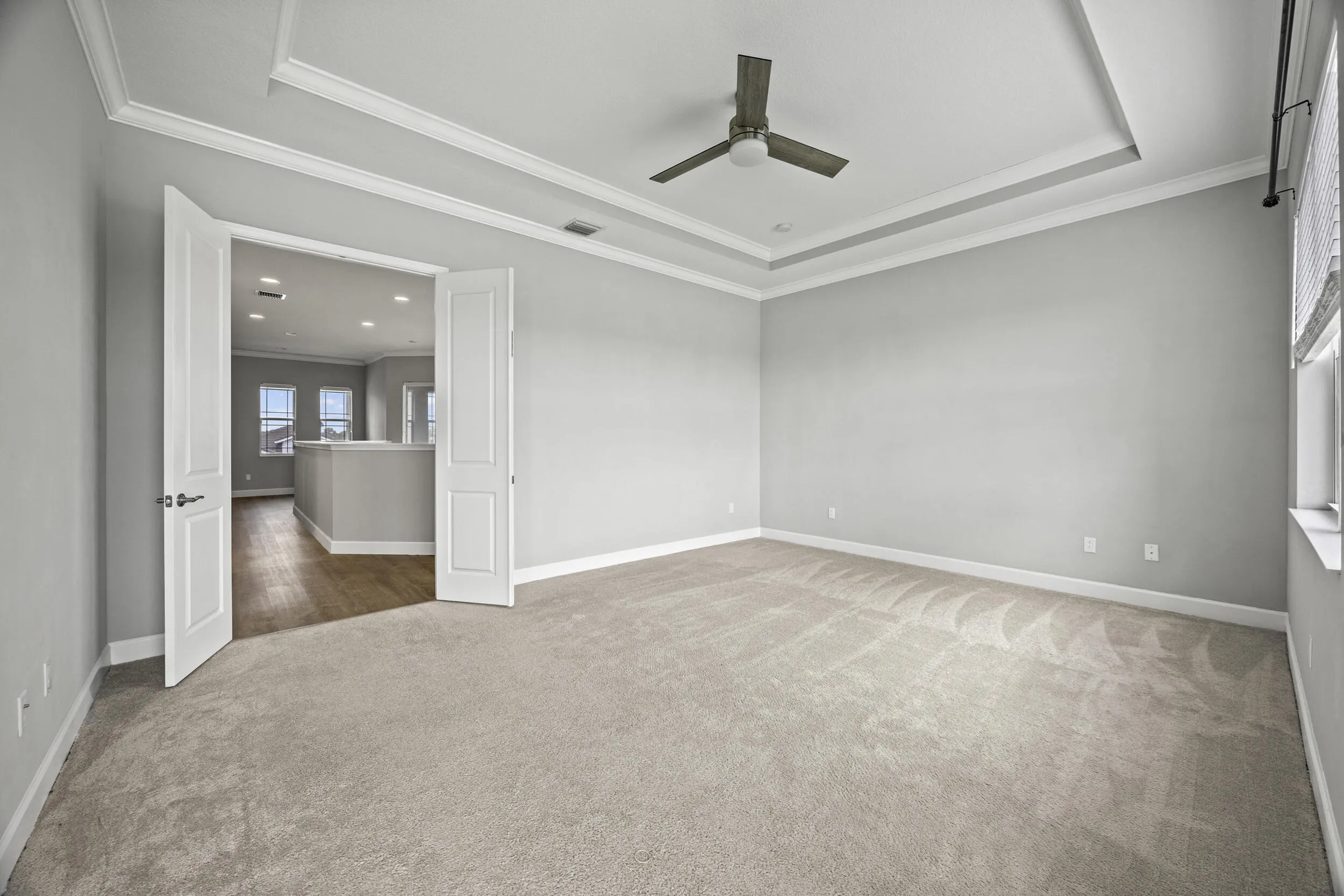 Tray ceiling with crown molding, carpeted flooring, double doors, ceiling fan, and window