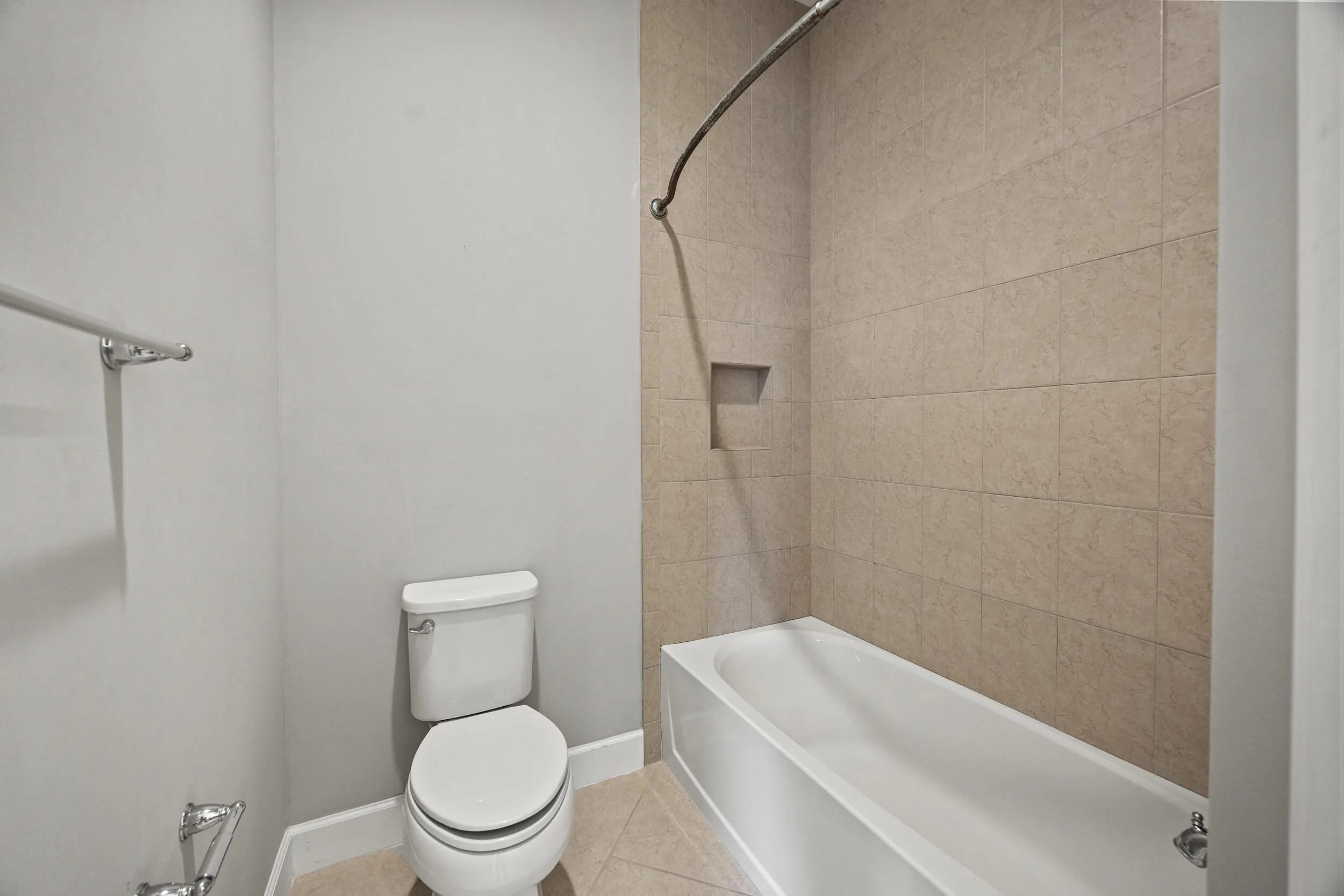 Bathtub with integrated shower, tiled walls, recessed shower niche, and floor-mounted toilet