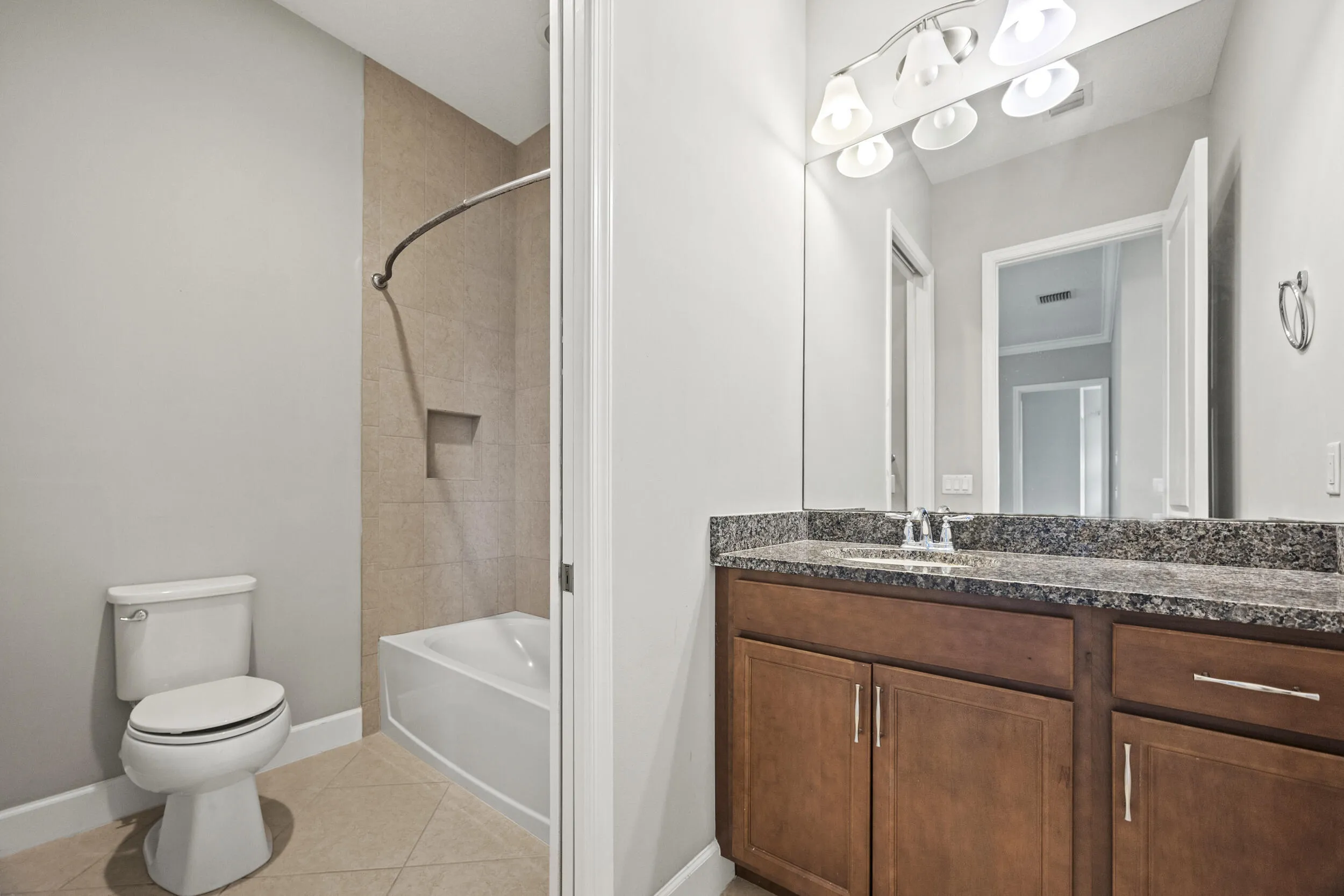 Bathroom featuring a tiled shower surround with built-in niche, a white tub, a vanity with a dark speckled countertop, wood-finish cabinetry, and a chrome faucet