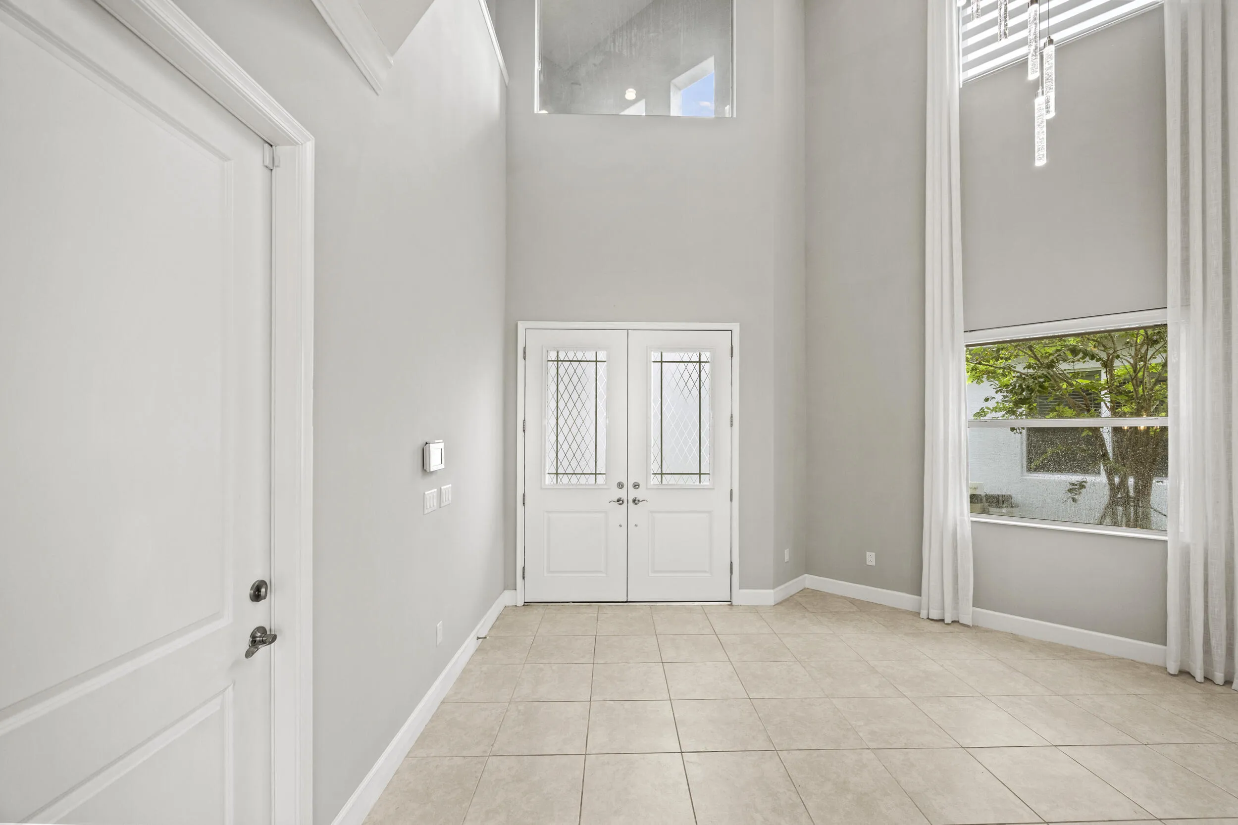 Grand entry with double front doors featuring decorative glass inserts, soaring ceilings, and a tall window