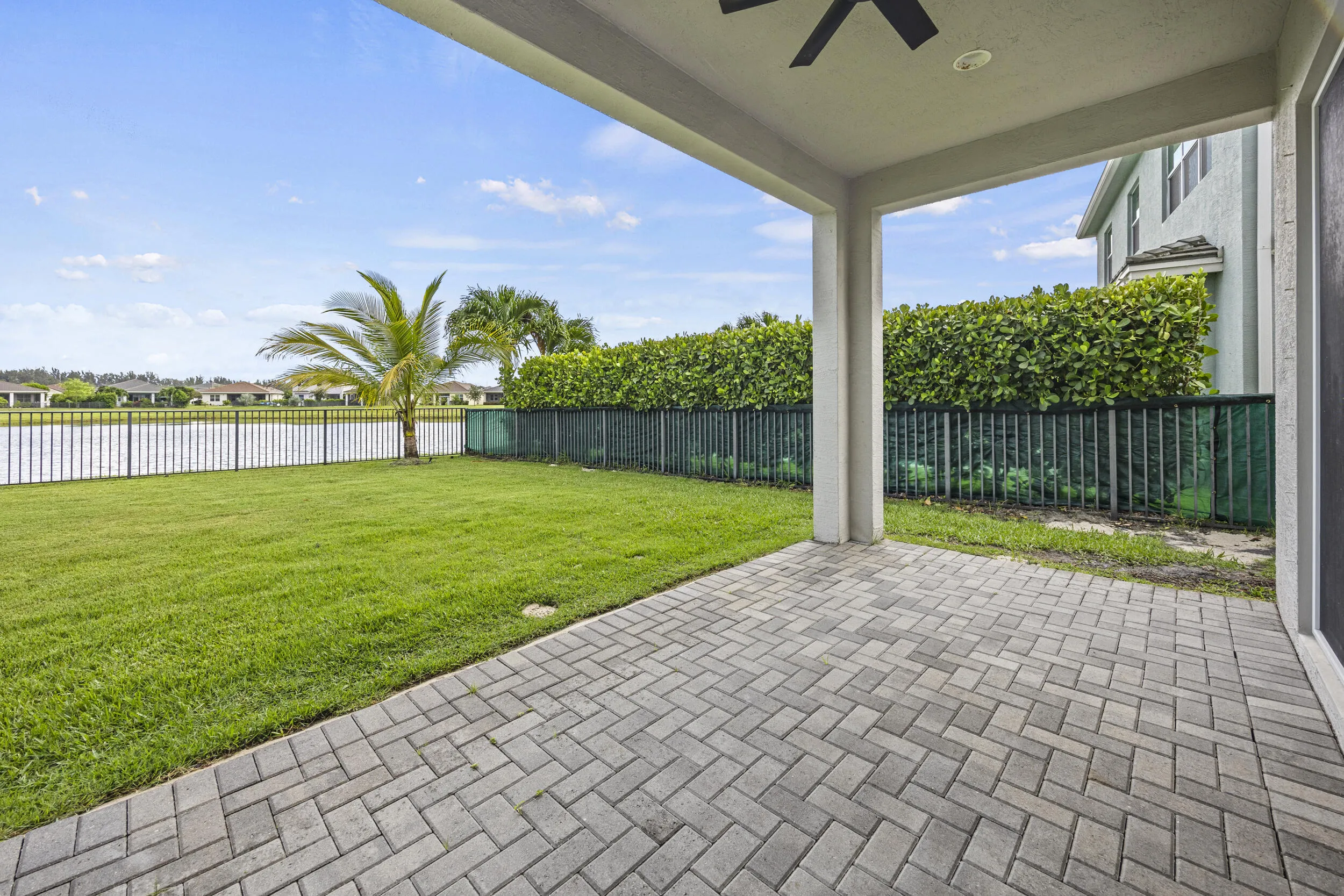 Expansive paver patio with covered overhead, leading to a manicured lawn and water frontage