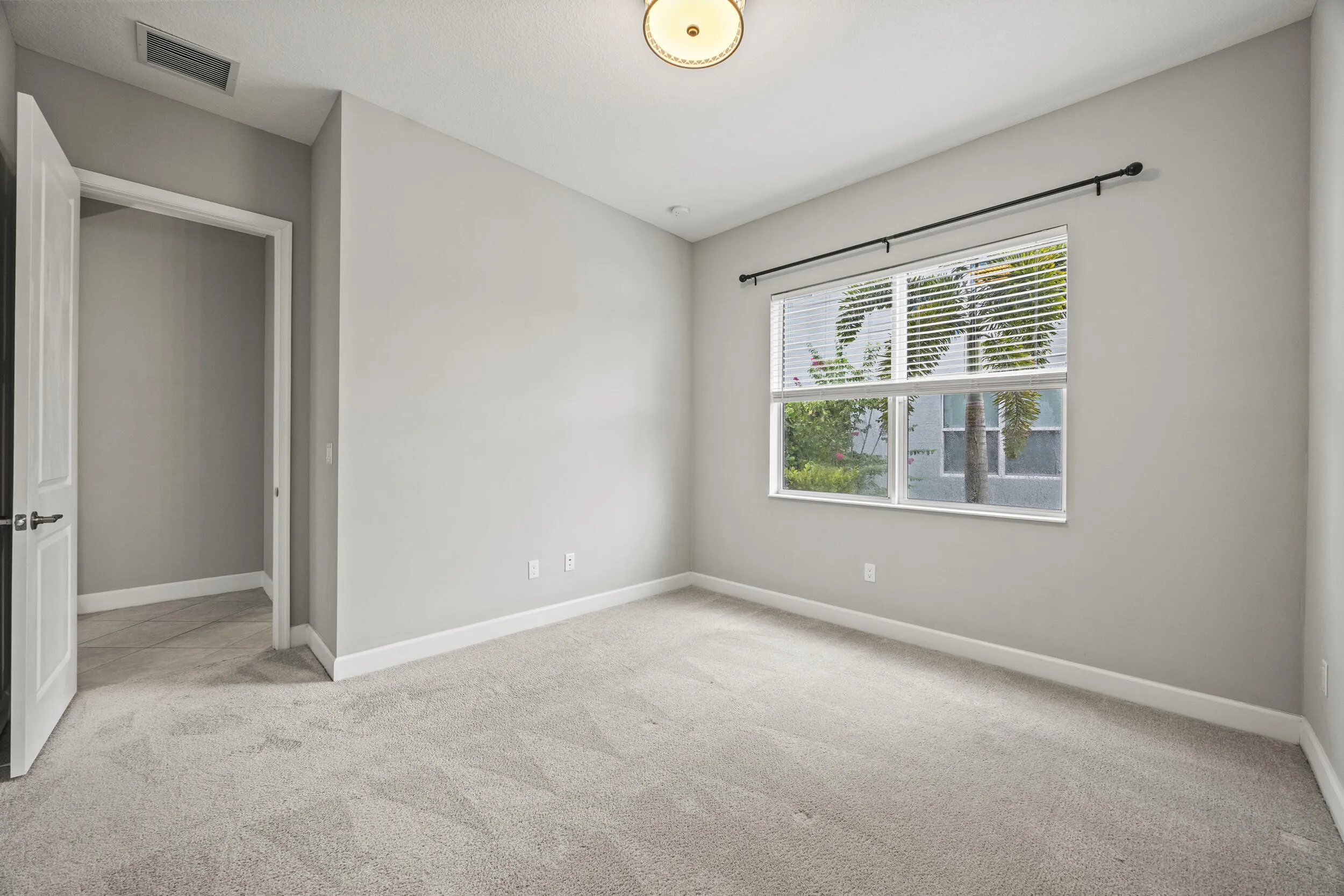 Neutral wall paint, carpet flooring, a window with horizontal blinds, and a flush mount ceiling light