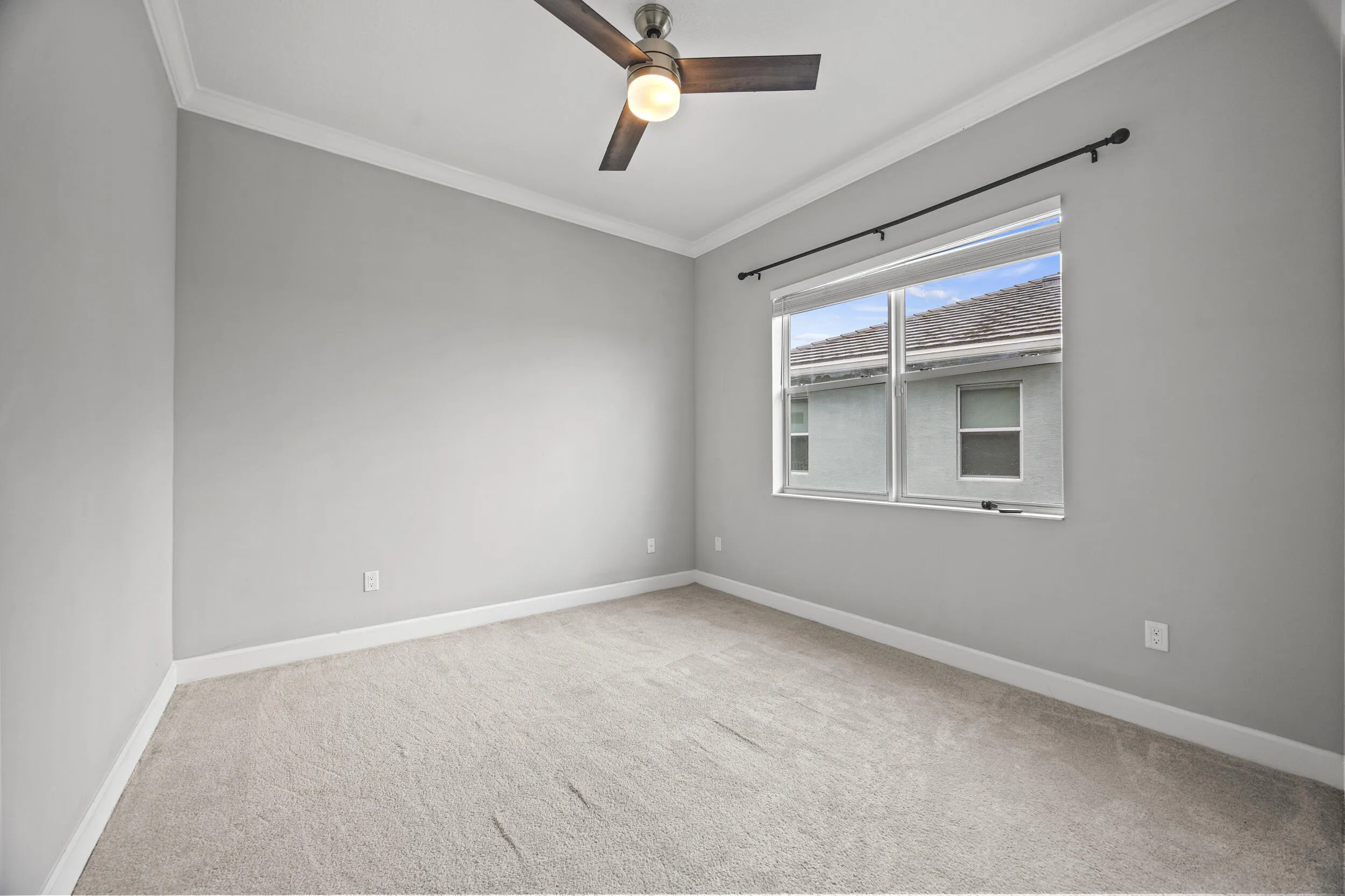 Recessed lighting, crown molding, gray painted walls, window with roller shade, and ceiling fan with light fixture
