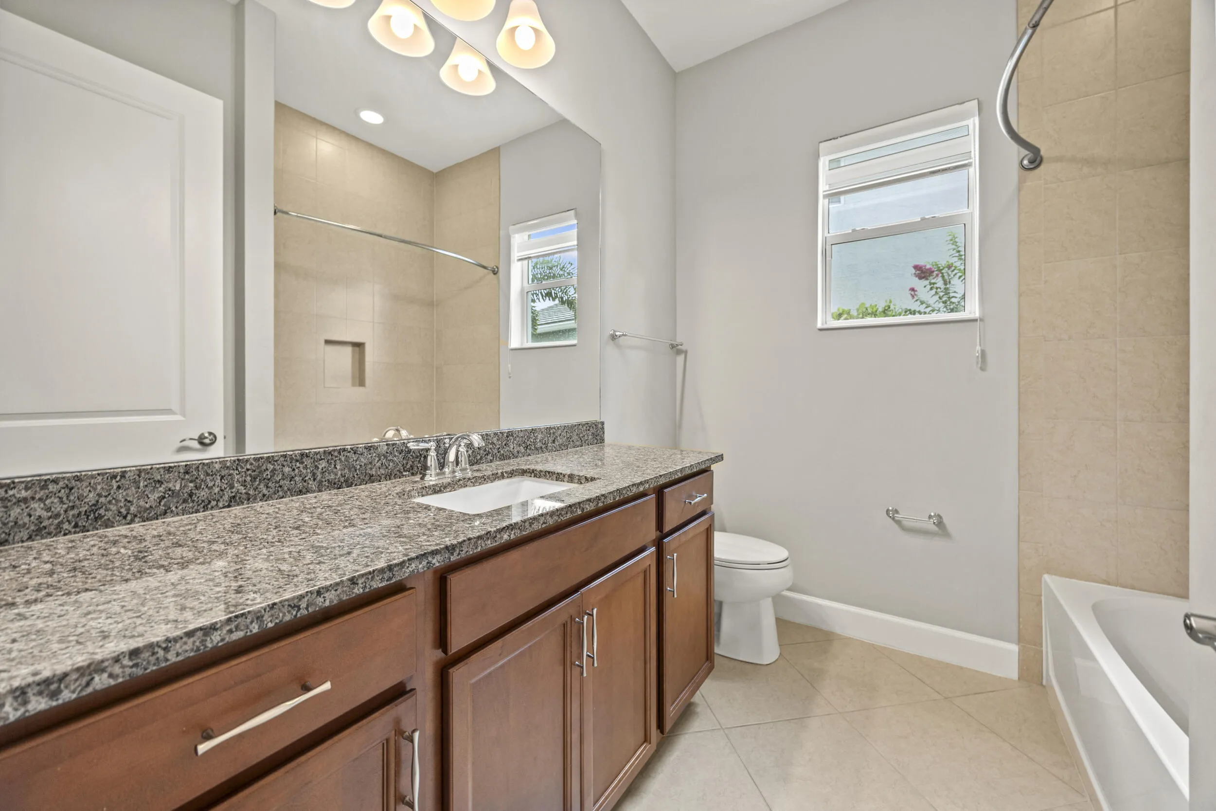 Dual-sink vanity with a stone countertop, wood-finish cabinetry, and tiled flooring